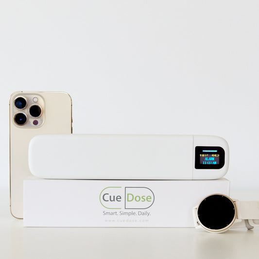 Cue Dose pill organizer with digital display held by a hand in a wellness setting.